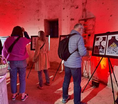 Wnętrze oświetlone na czerwone. Osoby oglądaja wystawe na sztalugach