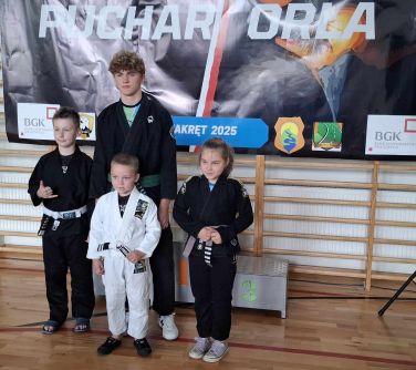 Jasna hala sportowa. Cztery osoby w kimonach stoi przed podium