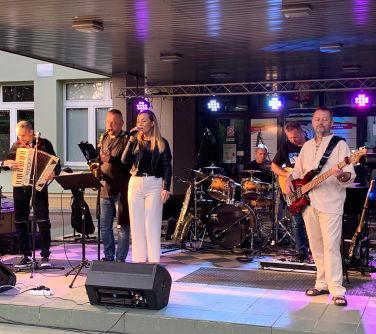 Na dworze. Scena przed wejściem do szkoły. Muzycy grają na instrumentach, po środku do mikrofony śpiewa wokalistka.