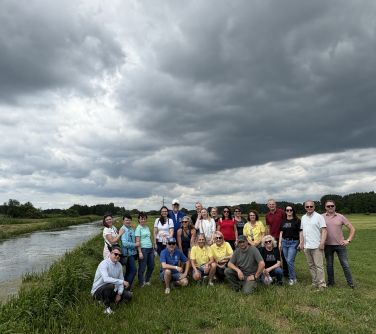 Pochmurny dzień. Na trawie zdjęcie grupowe. Po lewej płynąca rzeczka. W dalszym tle drzewa