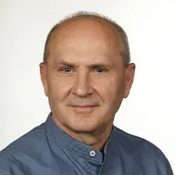 Mężczyzna w średnim wieku o krótkich, jasnych włosach ubrany w granatową koszulę z kołnierzem typu stójka.