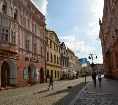 Ulica z brukowaną nawierzchnią otoczona kolorowymi, historycznymi kamienicami i kilkoma przechodniami.