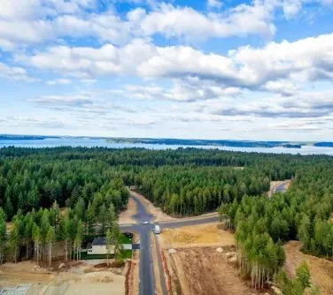 Skrzyżowanie dróg otoczone lasem iglastym z widokiem na odległe jezioro pod częściowo zachmurzonym niebem.