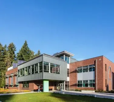 Nowoczesny budynek z czerwonej cegły i szarymi elementami elewacji na tle błękitnego nieba.