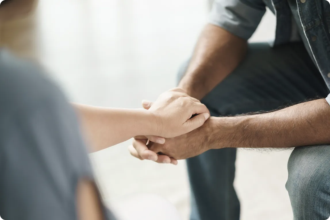 Dłonie dwóch osób trzymające się wzajemnie na tle jasnej powierzchni.