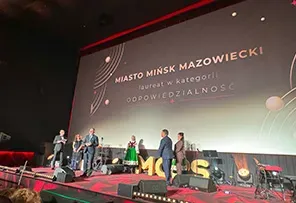 Scena z grupą osób odbierających nagrodę.  W tle dużu ekran z napisem „Miasto Mińsk Mazowiecki laureat w kategorii Odpowiedzialność”.
