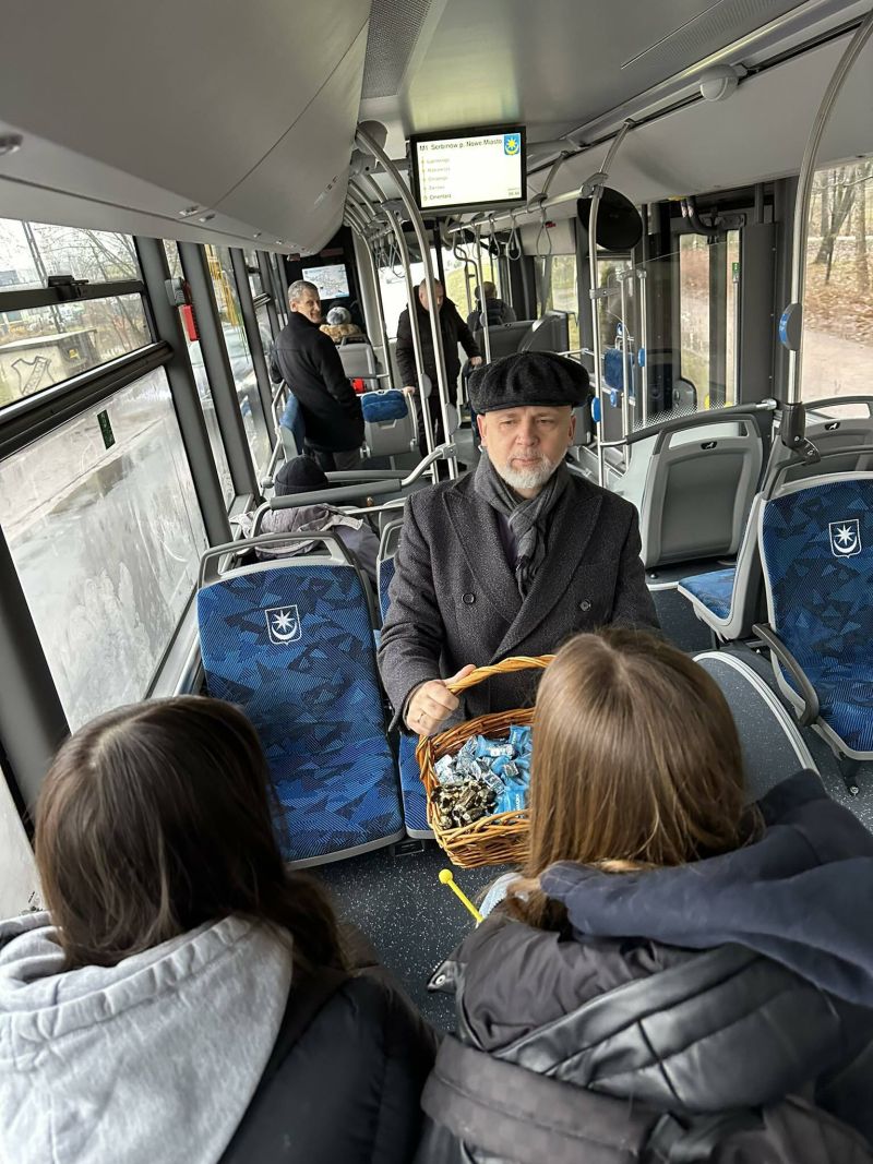 Wnętrze autobusu. Mężczyzna w berecie rozmawia z siedzącą kobietą