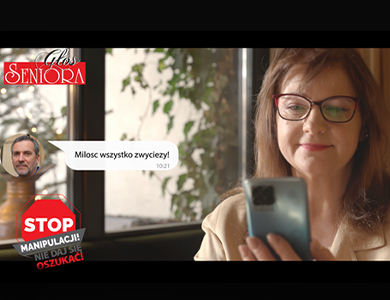 Zdjęcie uśmiechniętej kobiety która patrzy w telefon. W tle okno