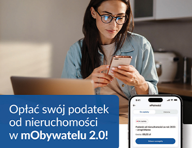 Kobieta w okularach siedzi przed laptopem. Patrzy w telefon