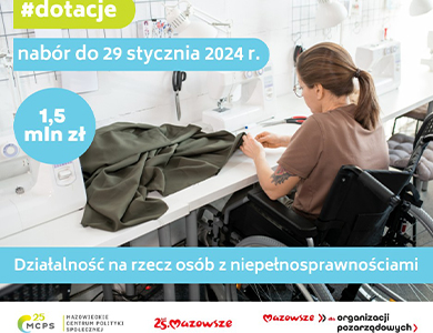 Kobieta na wózku inwalidzkim w koszulce z krótkim rękawem i włosami spiętymi w kucyk siedzi przy stole. Szyje na maszynie.