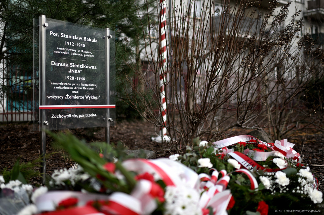 Na dworze. Wiązanki biało-czerwone leżą na ziemi przed szklaną tablicą