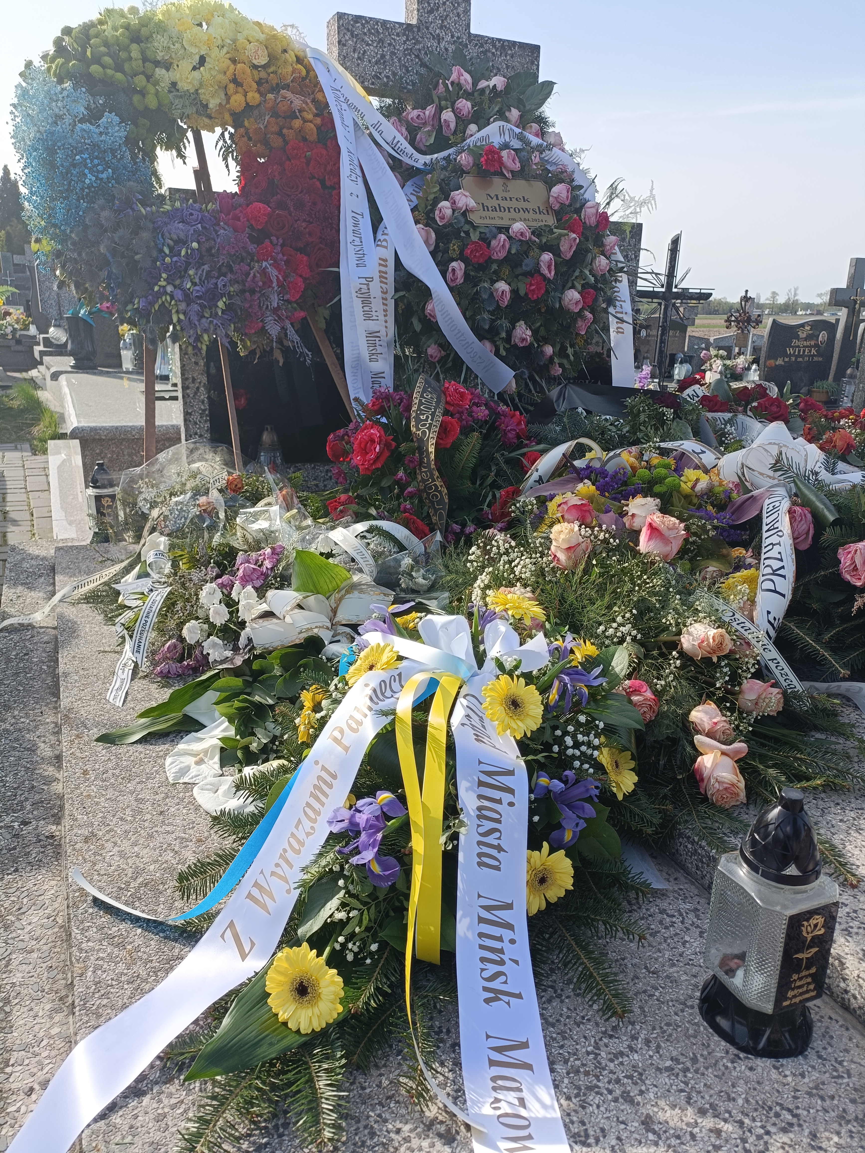Cmentarz. Grób murowany, na nim wieńce ze świeżych kwiatów.