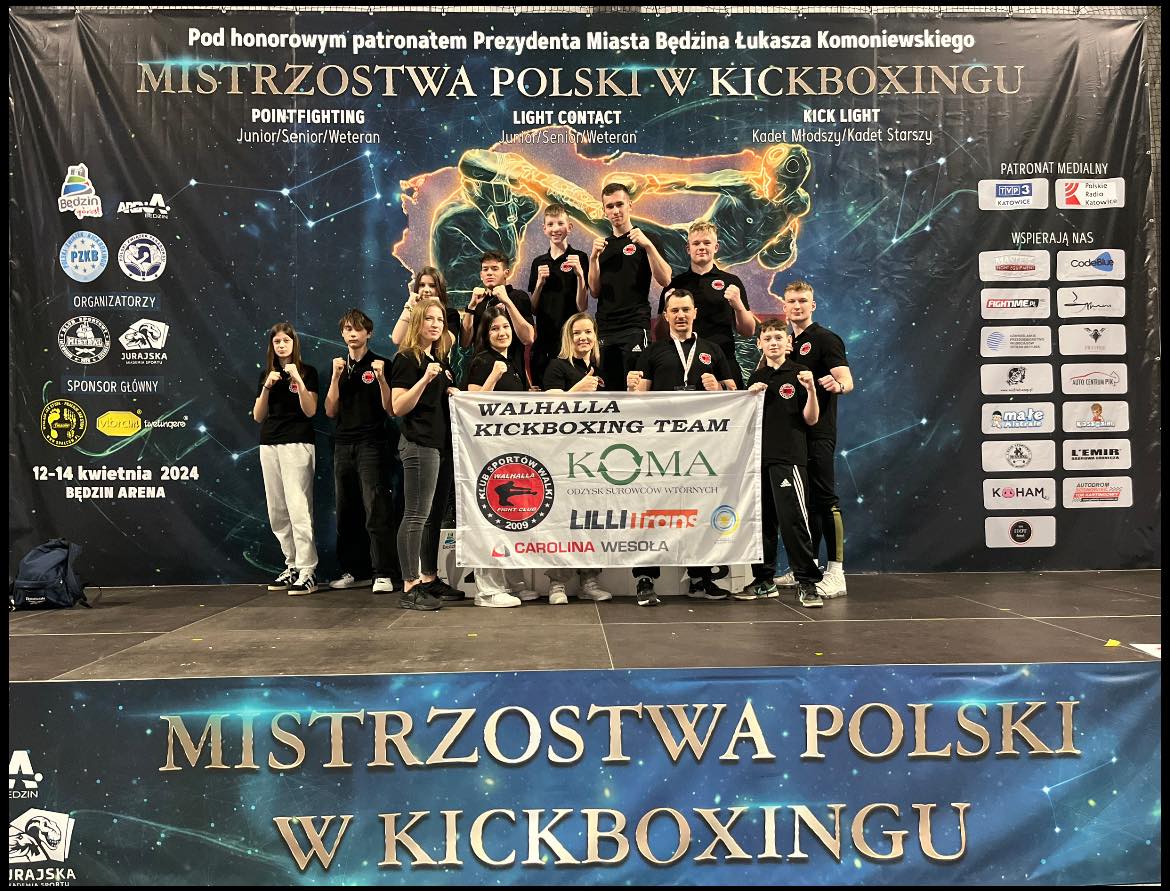 Grupa osób w sportowej pozie pozuje do zdjecia. Z przodu dwie osoby trzymają baner.