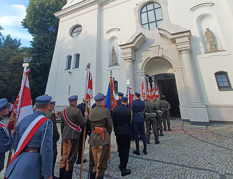 Na zewnątrz, poczty sztandarowe mundurowych stoją przed kościołem.