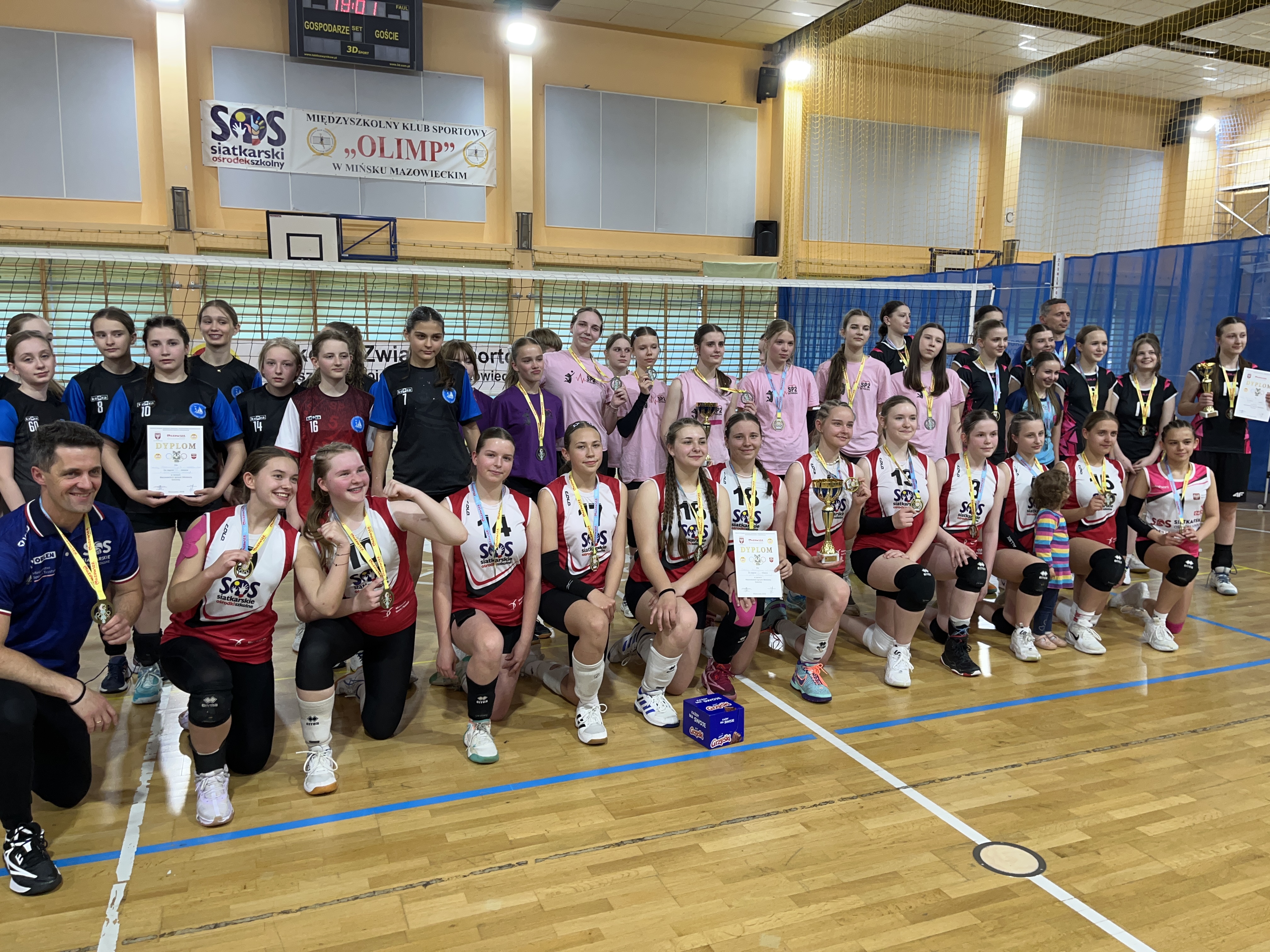 Wnętrze hali sportowej. Uśmiechnięte siatkarki w czerwonych koszulkach pozują do zdjecia.