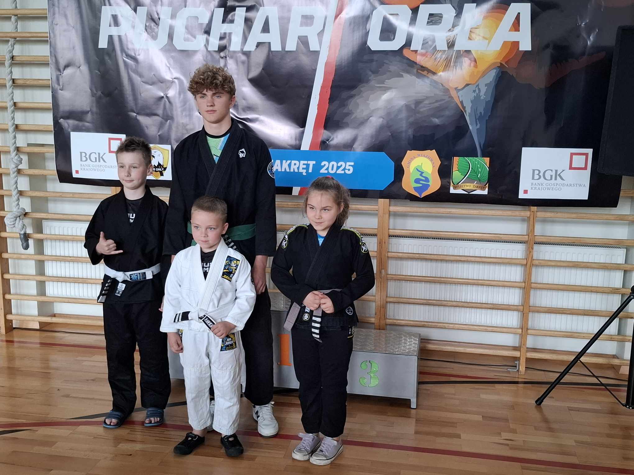 Jasna hala sportowa. Cztery osoby w kimonach stoi przed podium