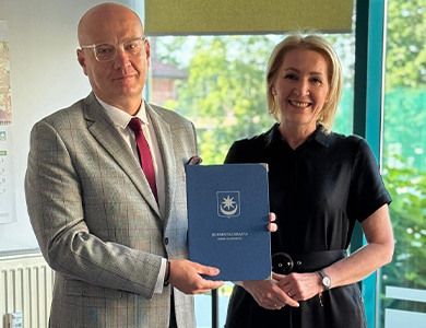Jasne pomieszczenie. Uśmiechnięta kobieta i mężczyzna. Mężczyzna trzyma granatową teczkę w dłoni.