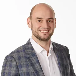 Mężczyzna w średnim wieku w białej koszuli i kratowanej marynarce uśmiecha się na białym tle.