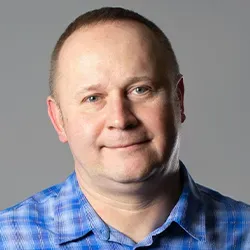 Mężczyzna w niebieskiej koszuli w kratę na szarym tle.