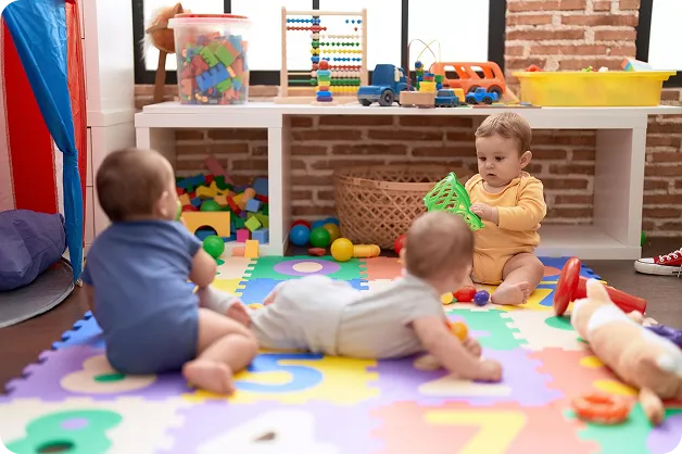 Trójka dzieci bawi się zabawkami na kolorowej piankowej macie w pokoju zabaw.